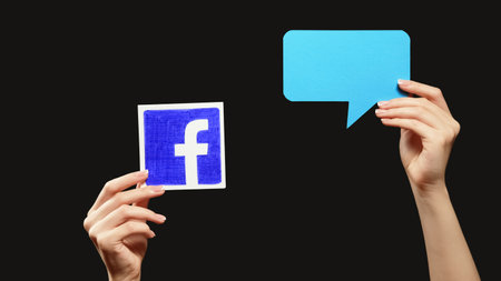 Kharkiv, Ukraine - May 12, 2020: Facebook message. Online chat. Female hands showing website logo blank blue speech bubble isolated on black empty space background.のeditorial素材