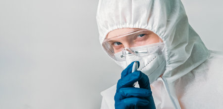 Healthcare virologist. Medical examination. Female doctor woman in white ppe suit pointing pen with watching you gesture isolated on grey background empty space.の写真素材