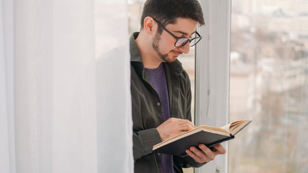 Reading leisure. Literature hobby. Home recreation. Serene dreamy man in glasses enjoying book bestseller story at weekend at window free space.の写真素材
