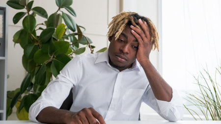 Work fatigue. Exhausted employee. Tired frustrated desperate business man depressed about stress overload sitting at desk in light modern office interior.の写真素材