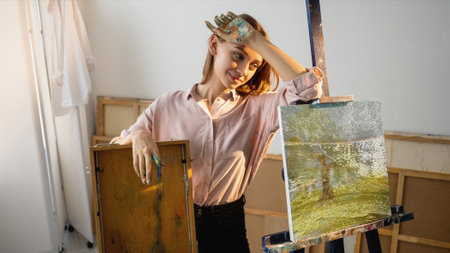 Nft painting. Crypto art. Blockchain technology. Satisfied tired female artist with glitch noise animated nature digital picture on canvas in studio.の写真素材