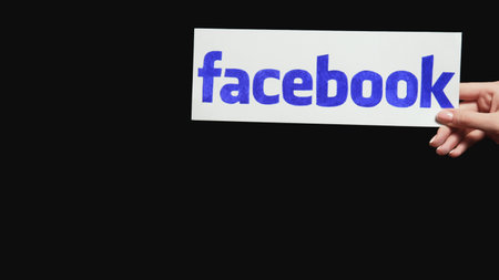 Kharkiv, Ukraine - May 12, 2020: Facebook logo. Social network influence. Female hands holding website sign on dark black empty space background.のeditorial素材