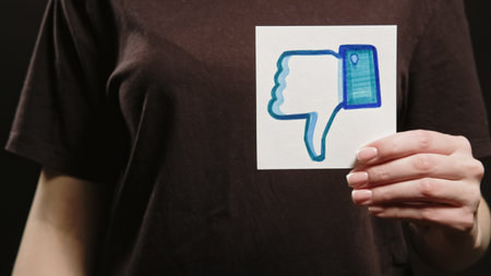 Kharkiv, Ukraine - May 12, 2020: Dislike sign. Social media unfollow. Negative feedback. Woman hand showing disapproving facebook thumb down icon on dark free space background.のeditorial素材