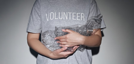 Plastic reduction. Zero waste. Volunteer woman in t-shirt with used creased bottles pile in hands recycling garbage in spotlight on gray background.の写真素材