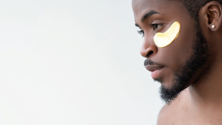 Male facial care. Skin rejuvenation. Handsome man with gold collagen gel eye patch on perfect radiant face isolated on white background empty space.の写真素材