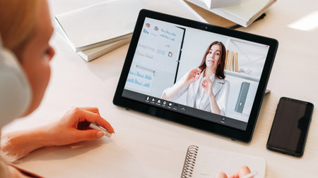 Video presentation. Online report. Business teleconference. Woman expert on tablet screen explaining charts graphs to female colleague at home workplace.の写真素材