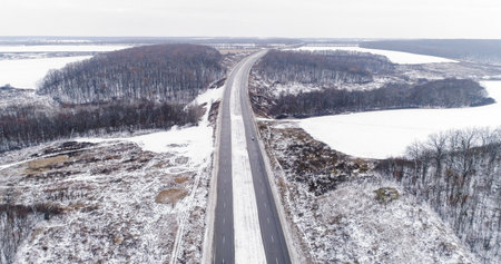 Aerial winter track. Snowy road. White frozen forest lakes cloudy day countryside asphalted driveway pavement cold season drone view.の写真素材
