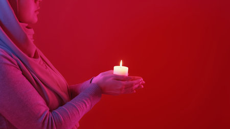 Ramadan praying. Islam religion. Unrecognizable woman hands holding burning candle flame light in...