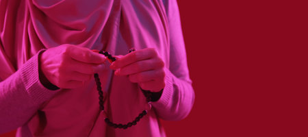 Beads praying. Tasbih tradition.Closeup of woman hands with wooden rosary islamic belief pink neon light on red copy space background.の写真素材