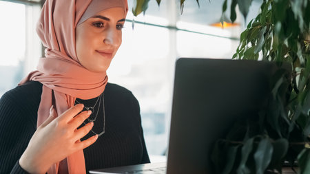 Video chat. Online work. Pretty smiling woman in hijab talking on laptop web conference digital...