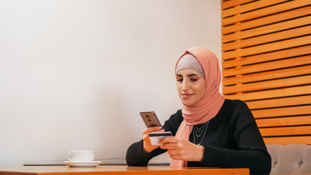 Online shopping. Mobile banking. Beautiful woman in hijab ordering buy on phone with credit card payment internet purchase at cafe copy space.の写真素材