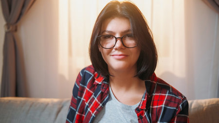 Happy woman. Smart look. Positive mood. Cheerful attractive female sitting on sunny shining living room interior.の写真素材