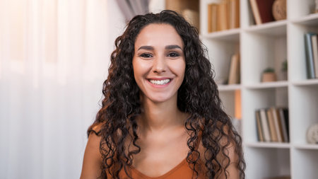 Happy face. Toothy smile. Optimistic attitude. Portrait of satisfied glad joyful cheerful pretty woman with dark curly hair at light home interior with free space.の写真素材