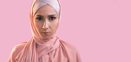 Muslim woman. Islamic face. Portrait of confident serious girl in hijab headscarf isolated on pastel pink empty space advertising background.の写真素材
