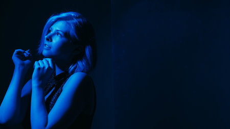 Hoping woman. Depression overcome. Female raising hands looking up expecting help mental mood disorder neon blue lights dark background empty space.の写真素材