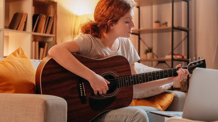 Guitar tutorial. Online acoustic training. Professional inspired musician woman teaching playing string instrument on laptop internet call at home.の写真素材