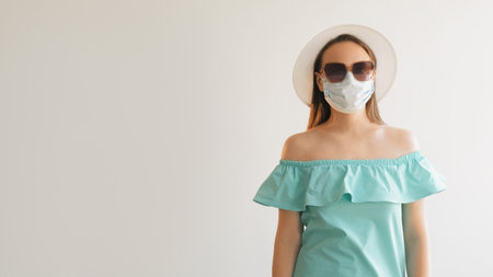 Pandemic time. Covid holiday. Girl in medical mask gloves summer dress sunglasses straw hat standing isolated on white empty space background.の写真素材