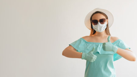 Coronavirus vacation. Girl recommending. Woman in medical mask gloves summer dress standing signaling thumbs up isolated on empty space white background.の写真素材