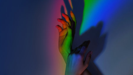 Rainbow touch. LGBT spectrum. Gay pride. Color inspiration. Tender female hands gesture in blur bright neon light gradient on free space blue shadow background.の写真素材