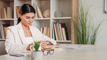 Information research. Female psychologist. Office work. Smiling elegant woman sitting desk reading...