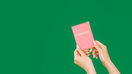 Passport service. Legal ID. Citizenship identification. Female hands holding official document in pink cover isolated on green empty space background.の写真素材