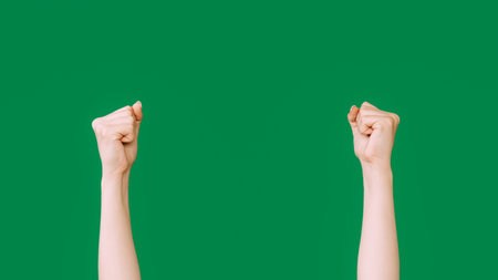 Raised fists. Protest gesture. Rebellion symbol. Female clenched hands striking knocking isolated on green empty space background.の写真素材