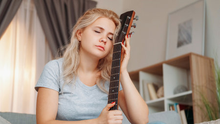 Lost muse. Upset woman. Guitar playing. Dreamful sad lady holding musical instrument feeling romantic sorrow sitting light room interior.の写真素材