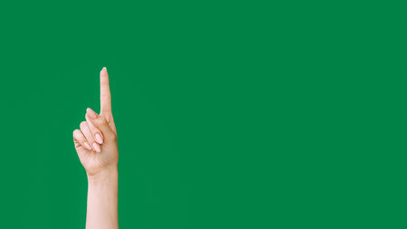 Pointing up. Idea gesture. Look here. Female hand index finger showing insight isolated on green empty space advertising background.の写真素材