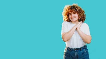 Joyful woman with curly hair smiling expressing pleased flattered emotion isolated on blue copy space background.の写真素材