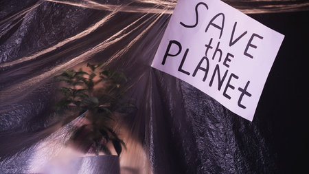 Nature conservation. Save planet. Environmental protection. Defocused silhouette with green plant behind wrinkled texture film with ecology banner on dark.の写真素材