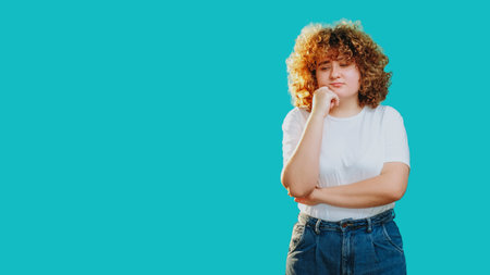 Pensive face. Hard decision. Confused doubtful puzzled girl with curly hair considering options isolated on blue copy space background.の写真素材