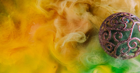 Christmas magic. Yellow smoke background. Shiny intricate Xmas bauble green mist cloud spreading on...