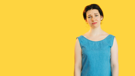 Sad disappointed woman in blue looking sad expressing melancholy isolated on yellow empty space background.の写真素材