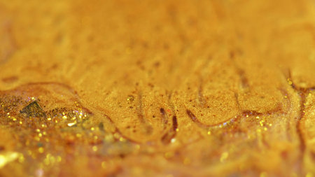 Shiny paint spill. Liquid glitter flow. Defocused golden color metallic sequin particles wet gloss acrylic fluid wave abstract art background with bokeh lights.の写真素材