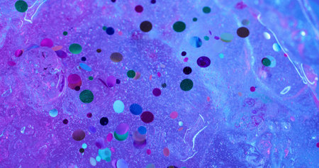 Shiny fluid. Confetti spill. Water with decorative sparks flows down purple ice surface. Festive colored defocused background with neon ink effect.の写真素材