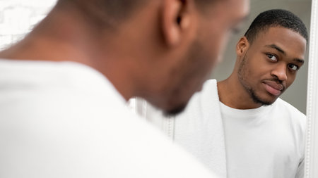 Morning routine. Facial care. Hygiene wellness. Handsome man with fresh face skin stubble white towel looking in mirror on light copy space background.の写真素材