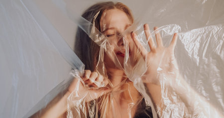 Suffering female. Breath hard. Sad depressed woman trapped behind wrinkled transparent polyethylene...