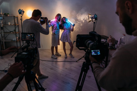 Futuristic posing. Neon girls. Women hold glowing bright decorative LED tubes. Ultraviolet lighting behind scene smoky video studio.の写真素材