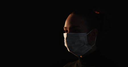 Quarantine silhouette. Covid protection. Respiratory disease. Dark outline of sick woman wearing face mask isolated on black copy space background.の写真素材
