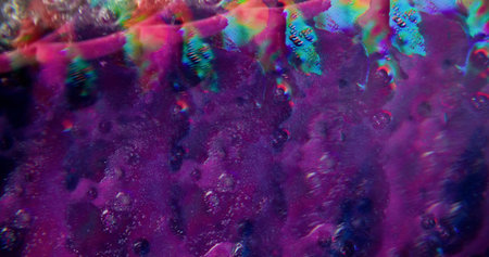 Colorful drip. Defocused drizzling background. Closeup sparkling purple water falling down glass on...