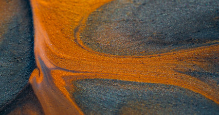 Glitter lava. Luxury paint. Precious liquid powder spill golden bronze yellow orange streams surface particles. Abstract gray mix wet defocused background.の写真素材