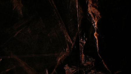 Distressed foil. Rust texture. Orange dark color light flare dust scratches surface on black uneven wrinkled abstract background.の写真素材