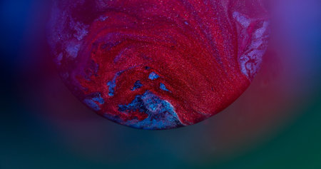 Ink pour. Colorful mix. Defocused red purple neon round texture flowing droplets glitter water spreading on abstract blue background.の写真素材