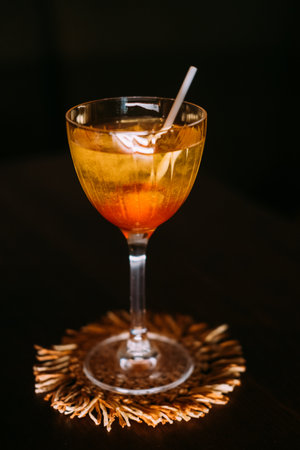 Sweet cocktail. Alcoholic mix drink. Yellow liquid served with orange lollipop in wineglass. Candy aroma beverage isolated on black.の写真素材