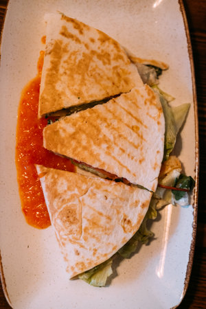 Pita sandwich. Cut burrito. Grilled stuffed flatbread served with vegetables on white plate. Tasty crunchy food with tomato sauce.の写真素材
