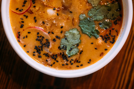 Sesame soup. Hot meal. Orange broth served with vegetable greens in bowl on wooden table. Tasty...