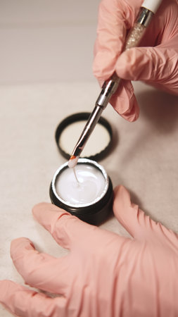 Fingernails gel. Acrylic hand manicure. Female beautician in gloves holding brush over nail polish mixing fluid getting ready for beauty procedure.の写真素材