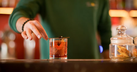 Garnishing beverage. Cocktail recipe. Barkeeper adding olive skewer to alcoholic refreshing drink. Aromatic negroni with tangerine peel.の写真素材