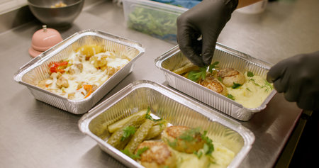 Packing takeaway. Restaurant food delivery. Chef hand garnishing served dish with chopped green....