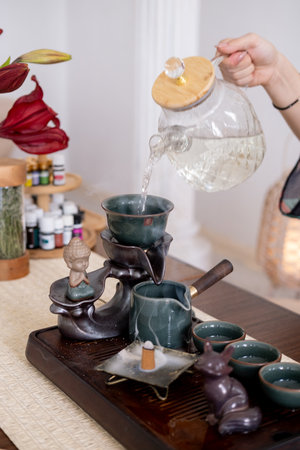 Water pouring. Tea ceremony. Woman hands filling glass teapot with drinking refreshing liquid...